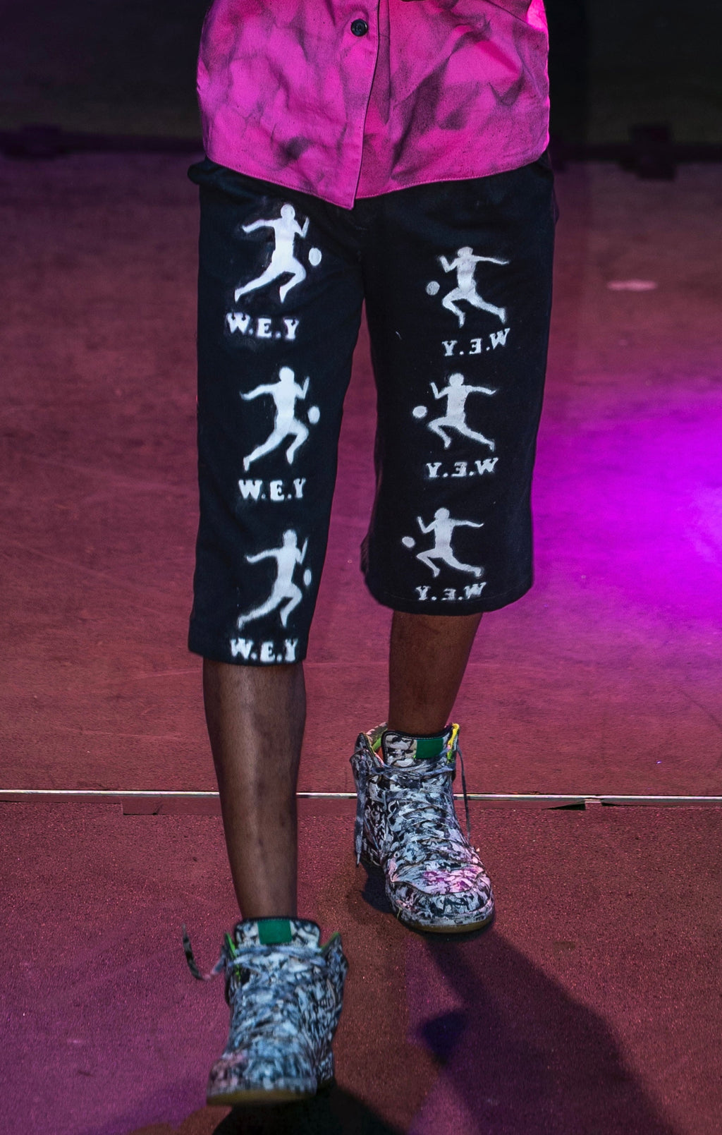 Person wearing a pink sleeveless top and black shorts with white graphics on a stage.