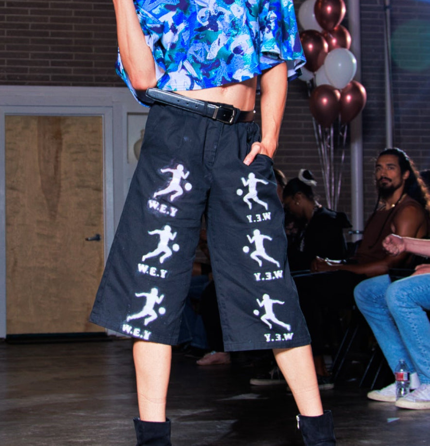 Model on a fashion runway wearing a blue floral top and black pants with white patterns.