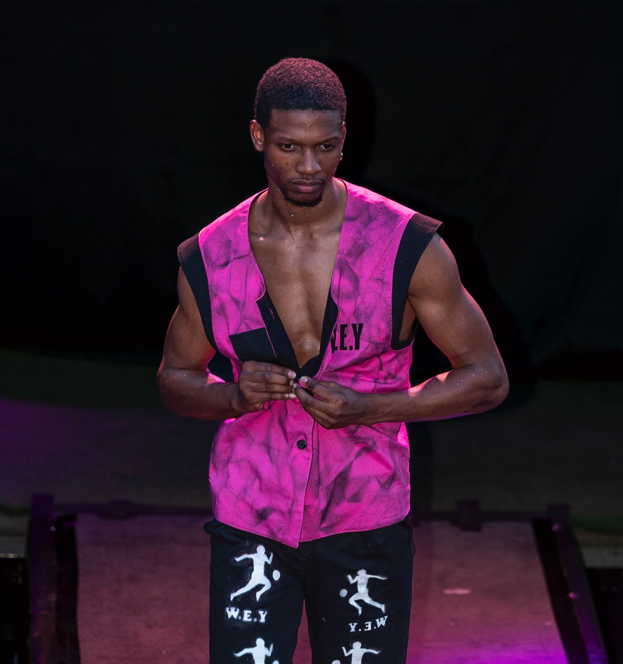 Person wearing a pink sleeveless top and black shorts with white graphics on a stage.