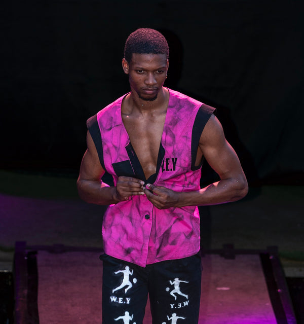Person wearing a pink sleeveless top and black shorts with white graphics on a stage.