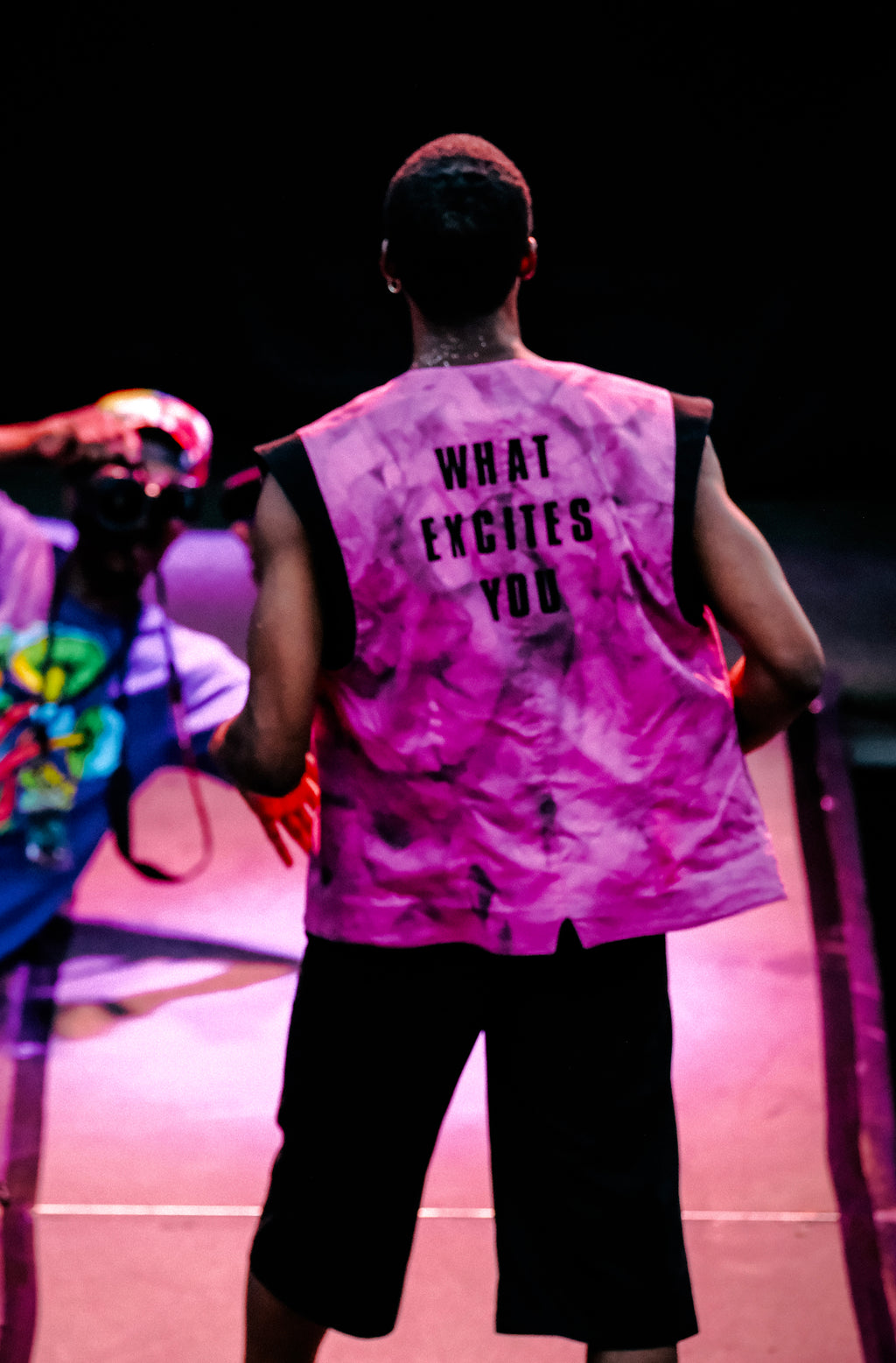 Person wearing a pink sleeveless shirt with text on the back, standing in a dark setting.