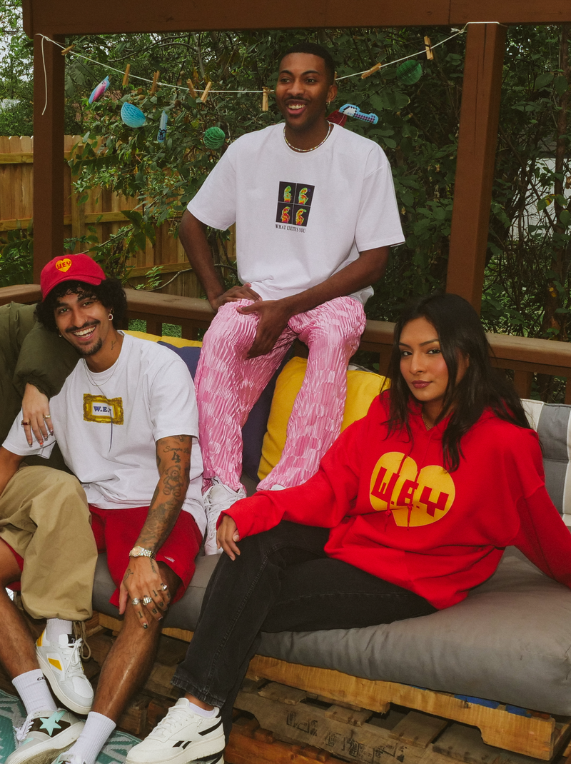 Group of people sitting on a wooden pallet bench outdoors, wearing branded clothing.